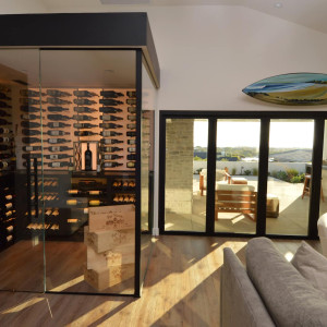 This home's glass wine room sits beautifully in the corner of its living room. Whether it's day or night, this is a stunning sight to see. Modern home glass wine cellar with glass door, glass walls, and ambient lighting